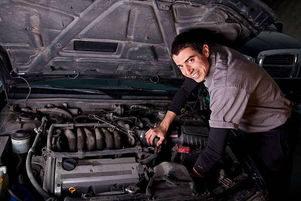 Smiling male auto repair mechanic works on an engine