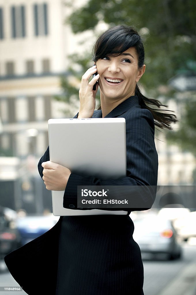 Businesswoman Holding computadora portátil conversaciones on Cellphone distrito financiero - Foto de stock de Actividad física libre de derechos