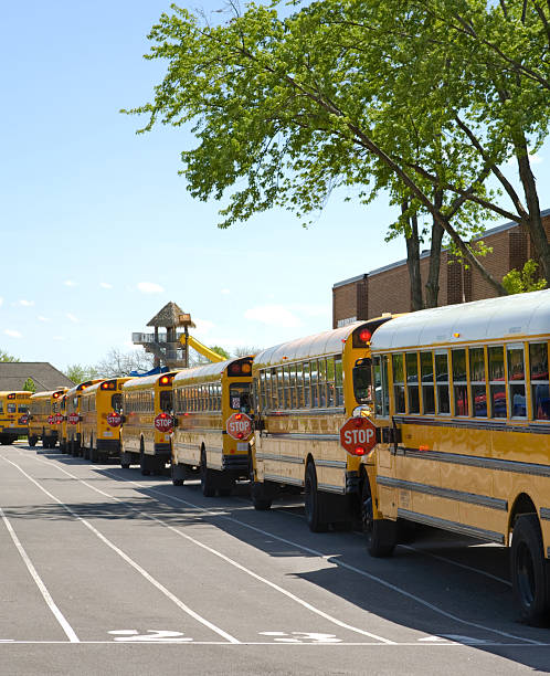 Horizontal shot of a line of parked yellow school buses under a cloudy sky.