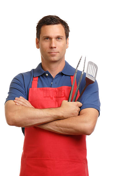 Thirty-something man in apron with barbecue utensils isolated on white.