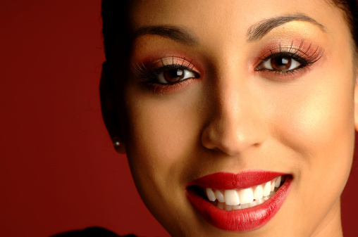 A beautiful mixed race woman smiles, African Heritage, red lips, false eylashes on red