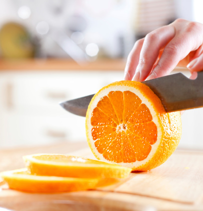 Woman's hands cutting fresh orange on kitchen