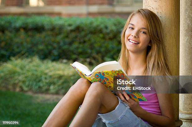 Teenage Schoolgirl Reading Textbook On Campus And Smiling Stock Photo - Download Image Now