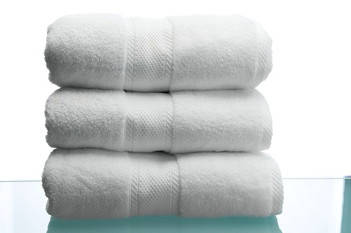 Three fluffy white bath towels stacked on a reflective, glass bathroom counter top http://www.erichoodphoto.com/istock/household.jpg
