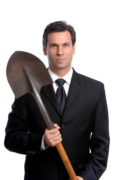 Businessman with Shovel Isolated on White Background A corporate VP prepares to break ground for the new medical center grave digger stock pictures, royalty-free photos & images