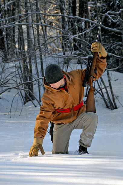 Hunter bent over in snowy woods tracking game. stock photo