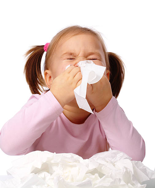 Young girl blowing her nose with pile of used tissues stock photo