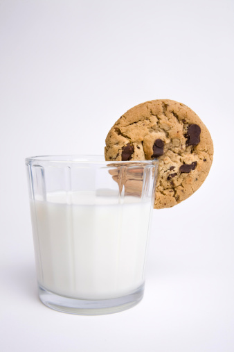 Elevated view of homemade chocolate chip cookies bowl and glass of milk on wooden table in domestic kitchen