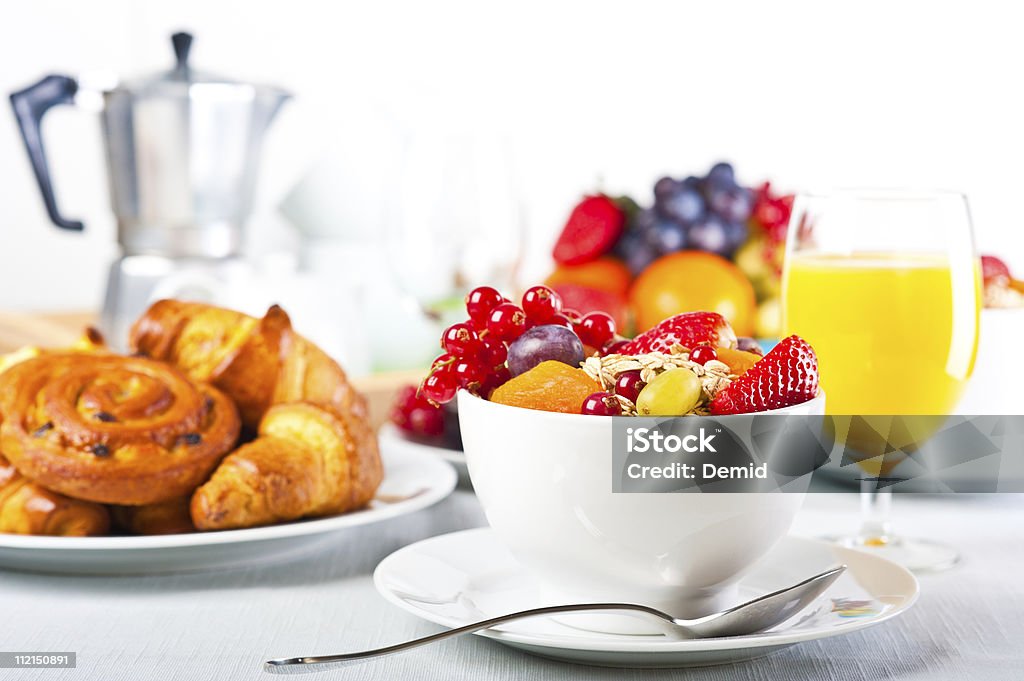 Bowl of fruit with glass of orange juice and croissants Table set up for continental breakfast: muesli, fruits and pastry. Continental Breakfast Stock Photo