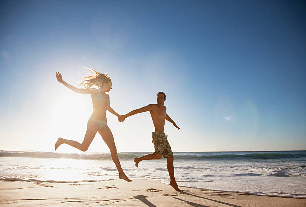pareja sosteniendo las manos y corriendo en la playa - swimming trunks bikini swimwear red fotografías e imágenes de stock