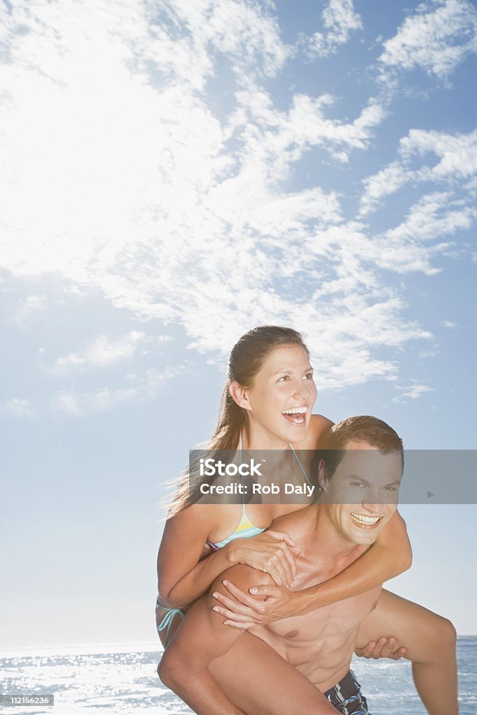 Playful man giving girlfriend piggyback ride on beach  20-24 Years Stock Photo