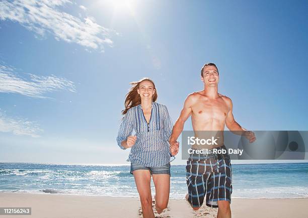 Coppia In Esecuzione Sulla Spiaggia Sorridente E Tenendo Le Mani - Fotografie stock e altre immagini di 20-24 anni