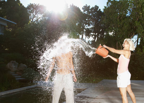 playful woman throwing bucket of water on boyfriend - temperatuur fotos stockfoto's en -beelden