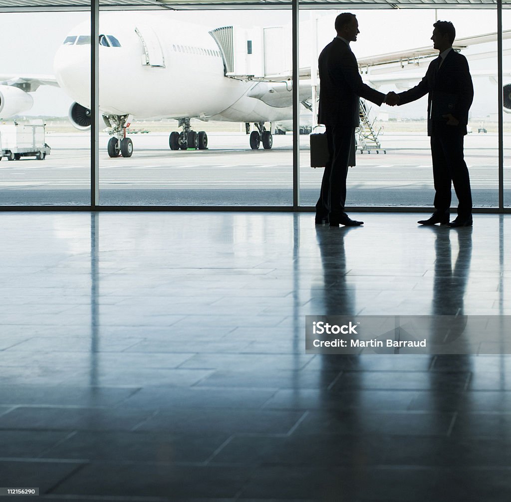Hombres de negocios estrechándose las manos en el aeropuerto - Foto de stock de Industria aeroespacial libre de derechos
