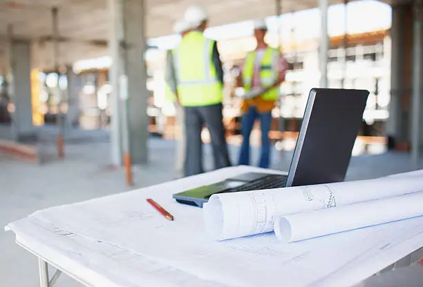 Photo of Construction workers behind blueprints and laptop on construction site