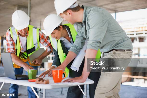 Trabajadores De La Construcción Mirando A Los Documentos En Solar De Construcción Foto de stock y más banco de imágenes de Solar de construcción