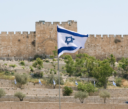Israeli flag flies with the wall surrounding the Old City of Jerusalem in the background.