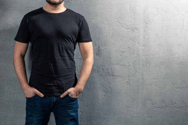 joven sano con camiseta negra sobre fondo concreto con copyspace para el texto. fotografía sin rostro de la modelo. - muscular build fotos fotografías e imágenes de stock