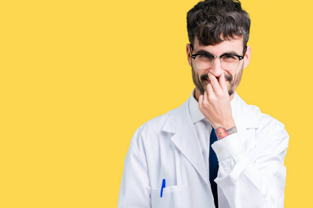 istock Young professional scientist man wearing white coat over isolated background smelling something stinky and disgusting, intolerable smell, holding breath with fingers on nose. Bad smells concept. 1124224205