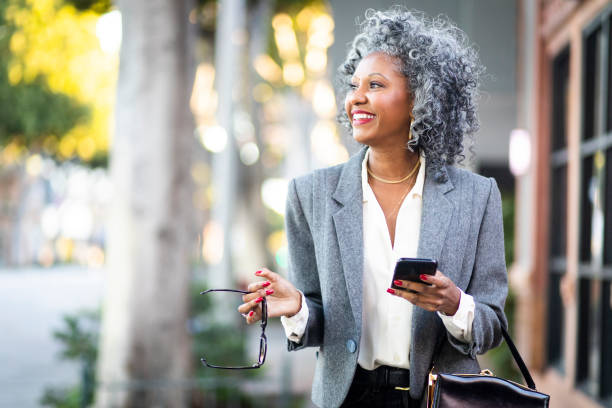 Mature Black Woman Texting While Walking in City An attractive black businesswoman on the town one mature woman only stock pictures, royalty-free photos & images