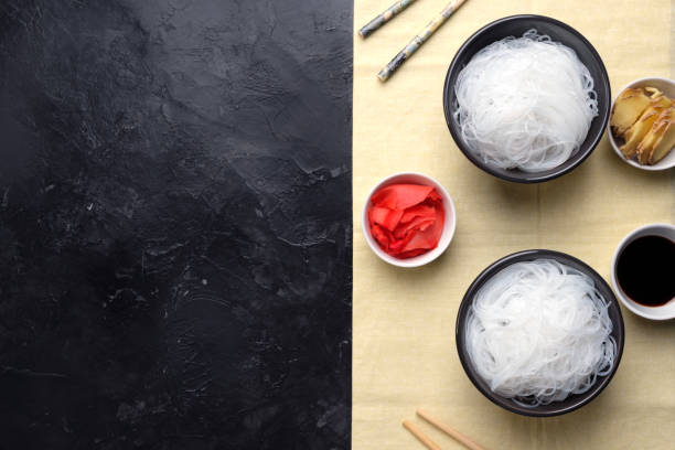 Chinese glass noodles with ingredients for cooking, vegetables and spices, ginger and soy sauce on black background top view