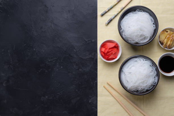 Chinese glass noodles with ingredients for cooking, vegetables and spices, ginger and soy sauce on black background top view