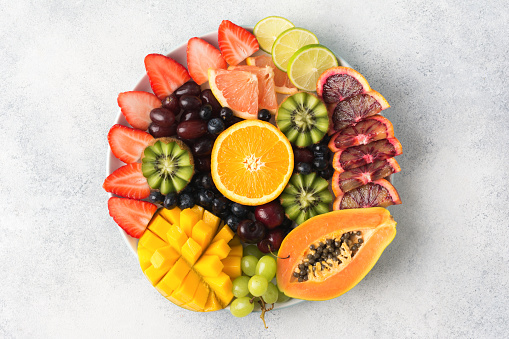 Healthy eating, assortment of raw fruits and berries platter on the off white background, top view, copy space