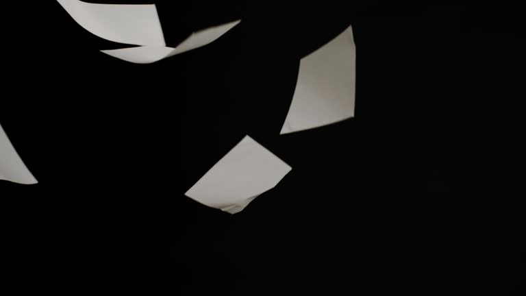 Pieces of white paper fall on a black background in slow motion.