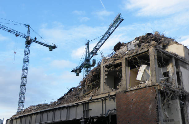 Yellow high reach excavator tearing down upper floors of old apartment block, crumbling facade and debris, concept of building demolition, urban redevelopment and construction industry.