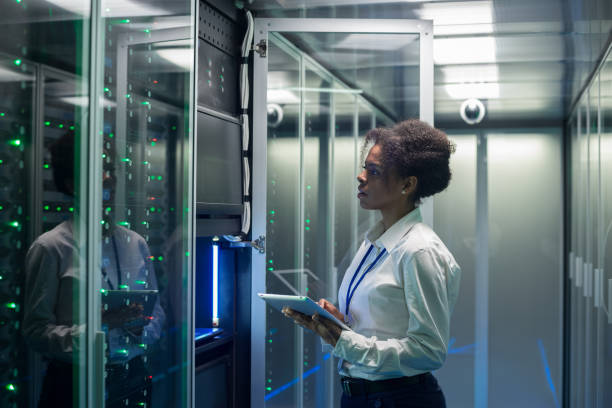 Female technician works on a tablet in a data center Medium shot of female technician working on a tablet in a data center full of rack servers running diagnostics and maintenance on the system medium shot stock pictures, royalty-free photos & images