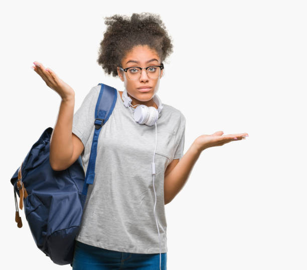 young afro american student woman wearing headphones and backpack over isolated background clueless and confused expression with arms and hands raised. doubt concept. - head and shoulders audio imagens e fotografias de stock