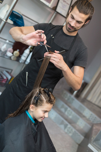 Girl at a hair salon with male hairdressers cutting her hair. About 10 years old, Caucasian brunette.
