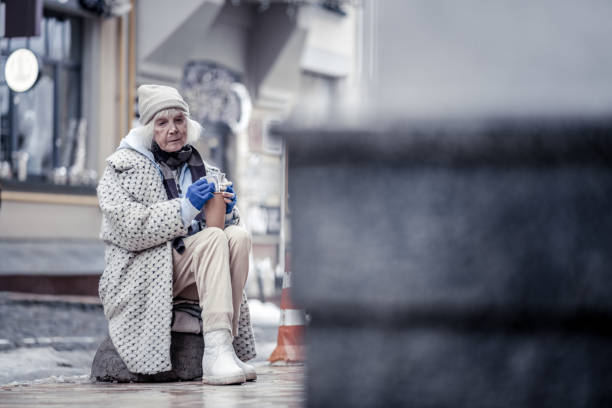 Middle of the street. Sad unhappy woman sitting on te stone in the middle of the street while begging for money