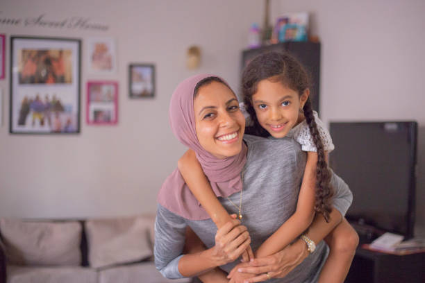 Hugging Mom A girl is climbing on her mother's shoulders. They are both smiling at the camera. egyptian ethnicity stock pictures, royalty-free photos & images