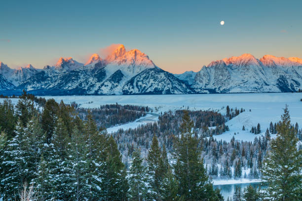 First Light on the Tetons A winter sunrise illuminates the Grand Tetons as a full moon sets in the west. snake river valley grand teton national park stock pictures, royalty-free photos & images