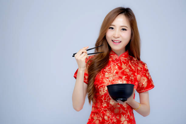 jovem mulher asiática retrato bonito vestir vermelho cheongsam segurando os pauzinhos e tigela isolado no fundo branco, conceito de feriado do ano novo chinês. - chopsticks human hand women isolated - fotografias e filmes do acervo