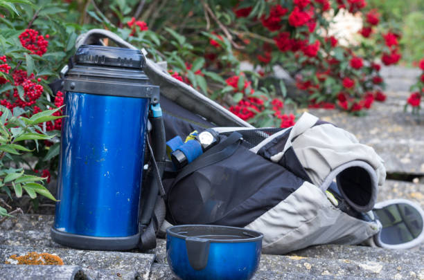 Thermos, backpack and headlamp. Tourist equipment. Cup with a drink. Fron view.