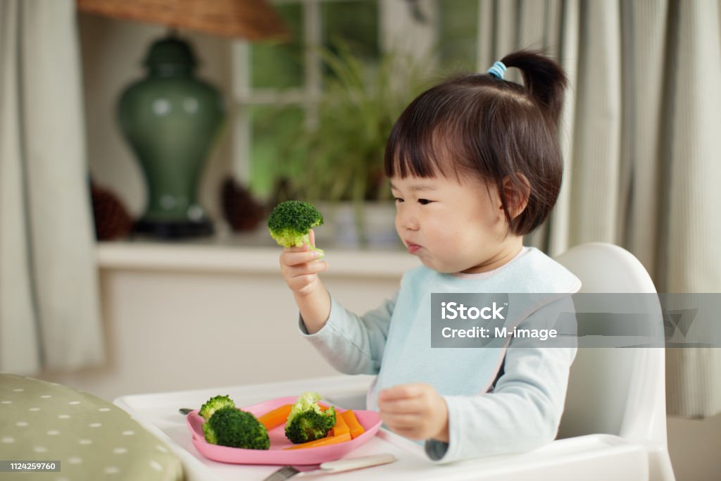 Kleinkind Mädchen essen gesundes Gemüse sitzen auf hohen Stuhl neben einem Esstisch zu Hause - Lizenzfrei Essen - Mund benutzen Stock-Foto