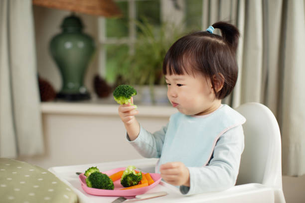 garota da criança comer vegetais saudáveis, sentado na cadeira ao lado de uma mesa de jantar em casa - asian meal - fotografias e filmes do acervo