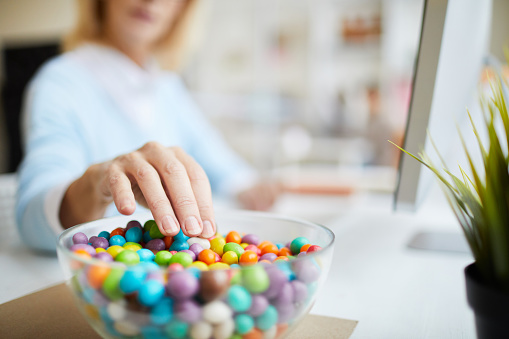 Primer plano de irreconocible empresaria sentado en la mesa y comer frijoles dulces mientras trabajaba en la oficina photo