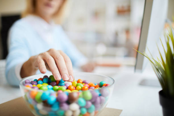 primer plano de irreconocible empresaria sentado en la mesa y comer frijoles dulces mientras trabajaba en la oficina - azúcar fotografías e imágenes de stock
