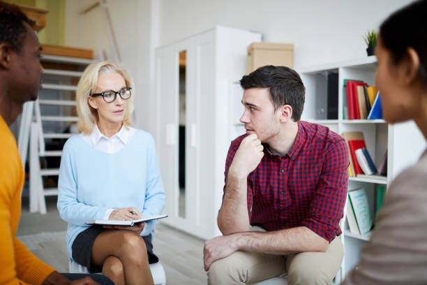 istock Content attractive lady psychologist in glasses sitting among young people with problems and making notes in diary while attentively listening to them during therapy session 1124270747