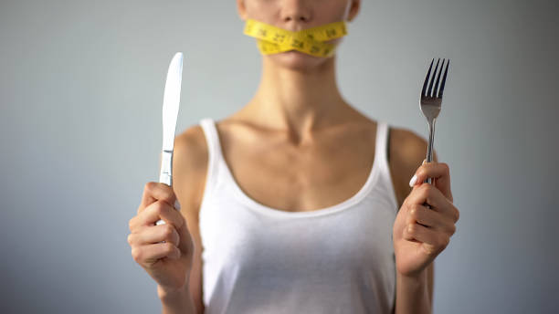 Anorexic girl holding fork and knife, mouth closed with tape, restrictions Anorexic girl holding fork and knife, mouth closed with tape, restrictions self destructive stock pictures, royalty-free photos & images