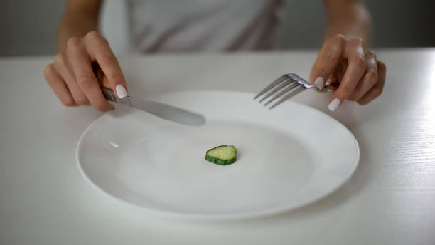 girl eating one small piece of cucumber, harming health, fear of overweight - anorexia imagens e fotografias de stock