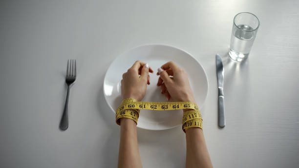 Hands tied with tapeline on empty plate, girl obsessed with counting calories stock photo