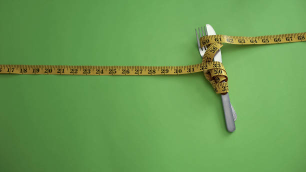 нож и вилка связаны измерительной лентой, понятие строгих ограничений питания - bulimia стоковые фото и изображения