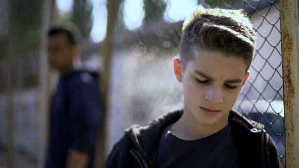 Upset teen boys leaning on metal fence, abandoned with society, orphanage Upset teen boys leaning on metal fence, abandoned with society, orphanage child arrest stock pictures, royalty-free photos & images