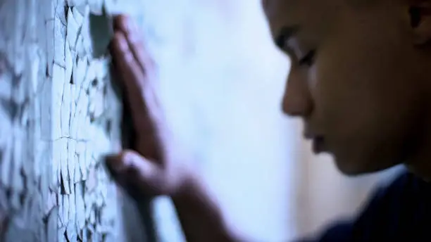 Photo of Afro-american teen touching flaky wall, poverty and life difficulties, sadness