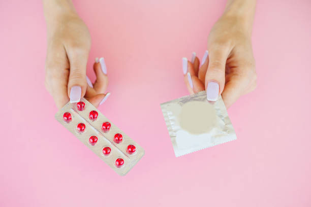 pills or condom. antibiotics from venereal diseases. concept of safe sex. pills and condom lie on a pink background - venereal imagens e fotografias de stock