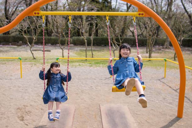 Two little sisters riding swing in playground